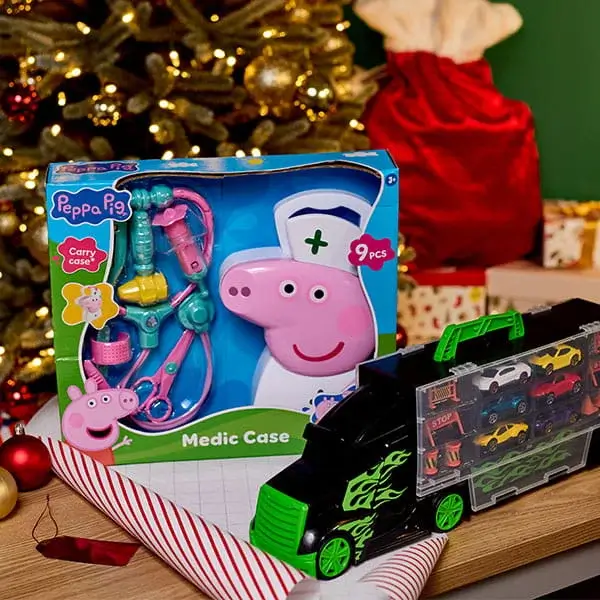 Children’s toy medical kit and toy car transporter displayed in front of a Christmas tree with festive decorations and wrapped gifts.